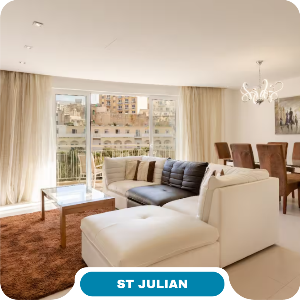 Bright, modern living and dining area with white sectional sofa, brown rug, glass coffee table, and large windows opening to a city view—ideal for short term rentals. “ST JULIAN” label at the bottom.